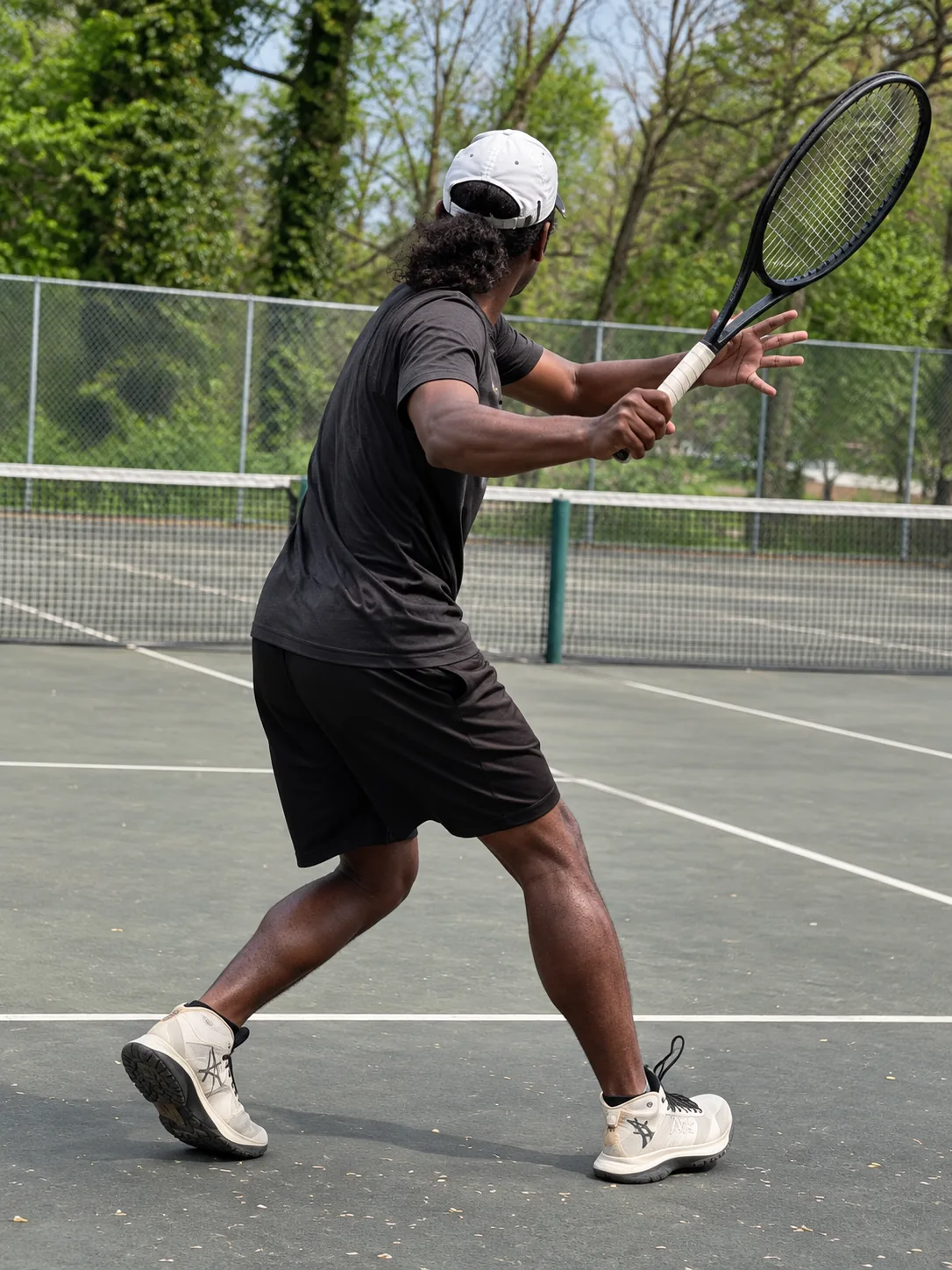 Perris Burke in a black shirt preparing a tennis shot on an outdoor court.