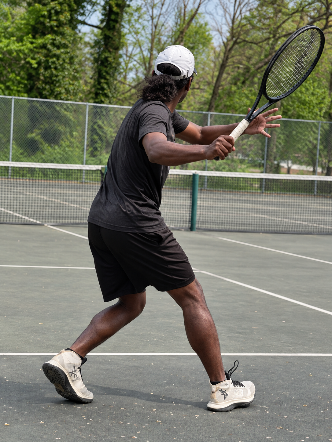 Perris Burke in a black shirt preparing a tennis shot on an outdoor court.